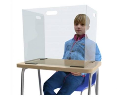 A boy sits a desk with a clear desk partion.