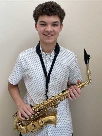 Photo of Gavin Purnell (11) holding his Alto saxophone in front of wall, he is smiling in the photo and very happy.