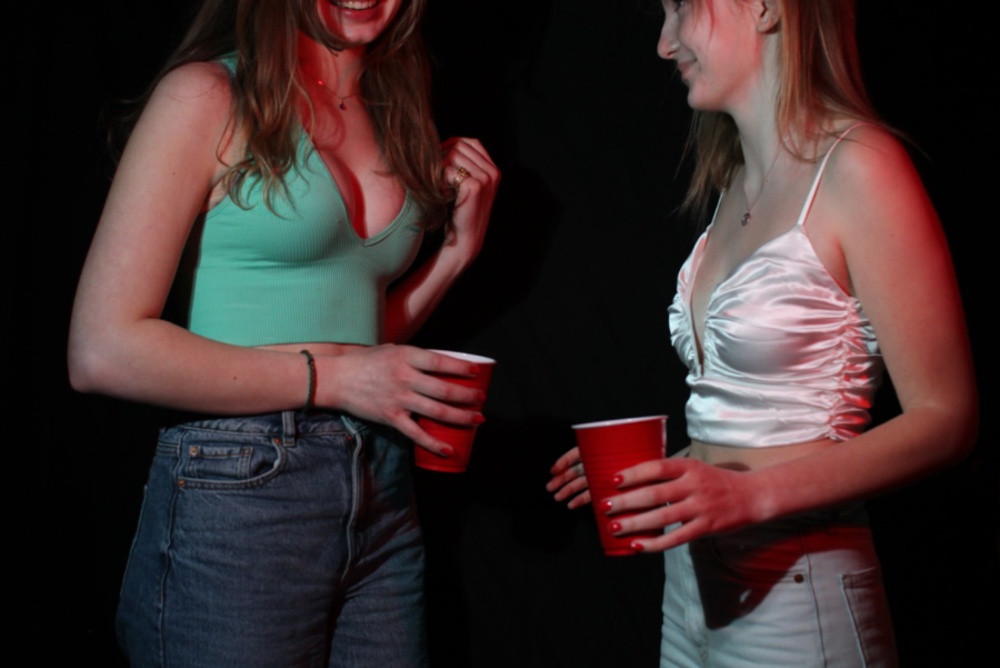 two girls with blonde hair hold red solo cups and talk