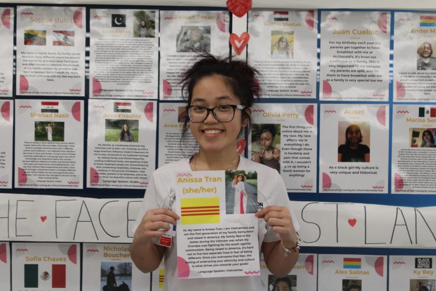 Holding her poster, Anissa Tran (12) poses in front of the Faces of East Lansing project. Tran is one of the 64 students who made portraits for the project.