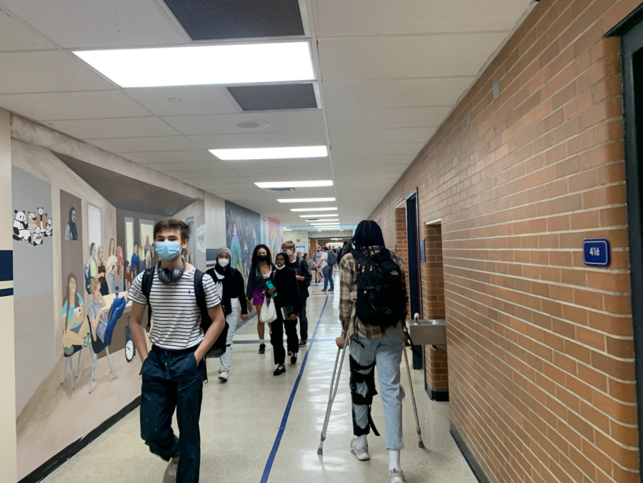 Students with mask walk in on in brick hallway with white tile floor