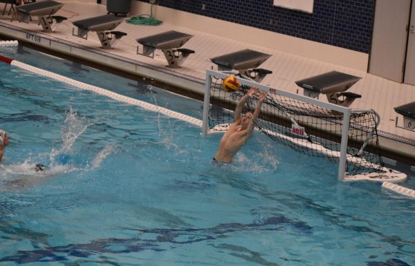 Tipping the ball just over the cross bar, goalie Nathan Thayer (11) makes a save at a boys water polo game.