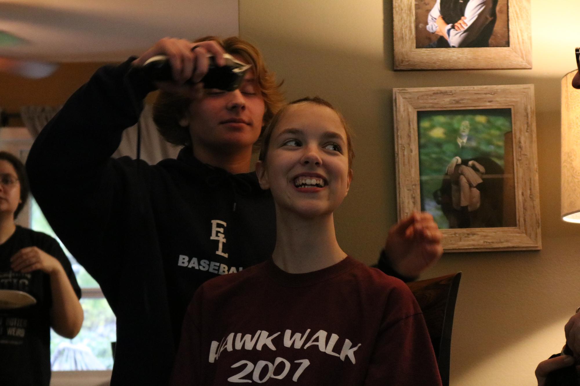Smiling , Kelly Maier (11) sits in her living room as Jesse Tuinstra (11) finishes shaving her head. Photo by Nick Acevedo