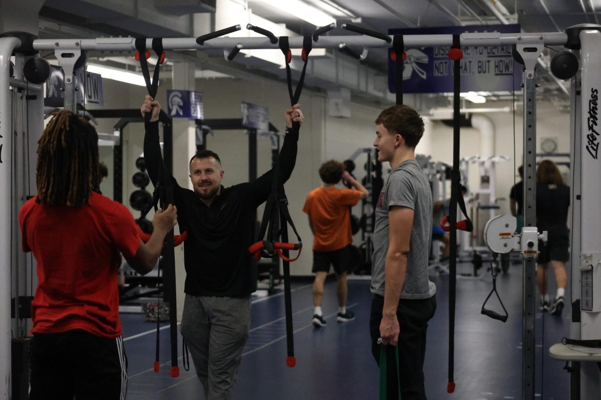 Coach Mike Kelley talks with two athletes during strength and conditioning after school on Feb. 2. 

