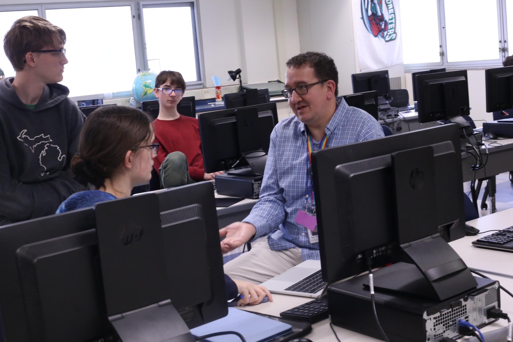 During Coding club, Orion Smith sits with students Kari Richards (11) Elliot Myers (12) and Tristan O'Keefe (9) about the possibility using Roblox Studio as a way to learn coding on 10/30. Photo by Joelle King