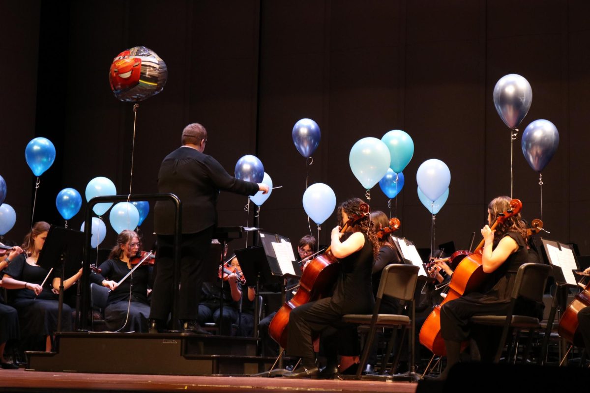 Orchestra students play onstage, decorated with helium balloons for the song, “Helium”. A Lightning McQueen balloon is front and center, highlighting the transportation theme. 