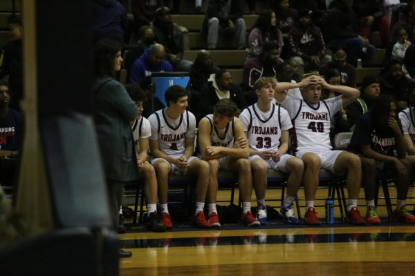 Sitting on the bench, players left to right Isaiah Lott (12), Benjamin Fletcher (12), Owen Fortman (12), Henry Peck (11), Paul VanDam (11) watch as their teammates face Kalamazoo Central at the Don Johnson Field House on March 6th, 2025. The Trojans dominated with a 77-42 final score.