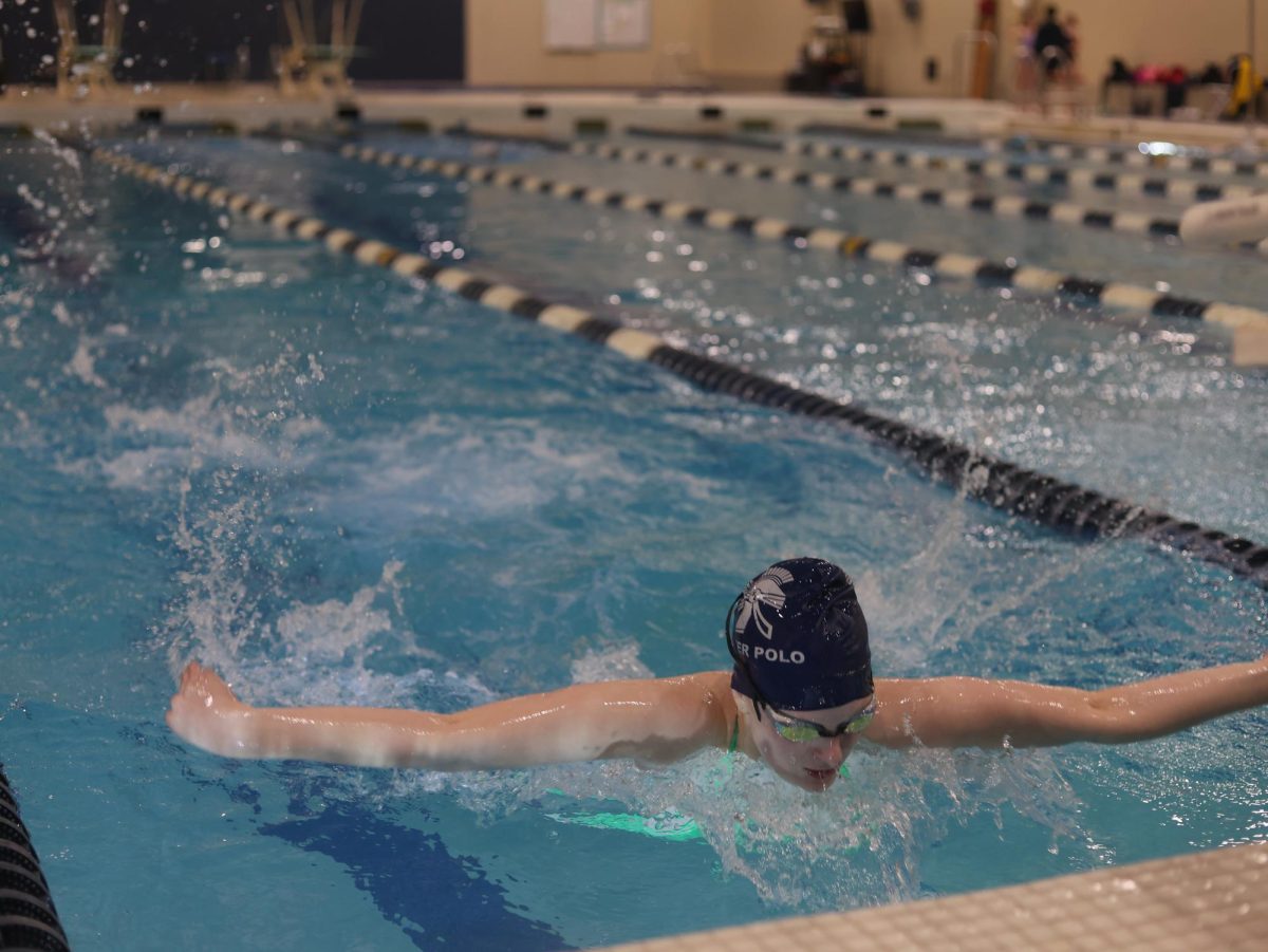 Executing the butterfly stroke, Sophie Bellon (11) swims down the sixth lane. Sophie wore a water polo swim cap, transitioning from one water sport to the next.