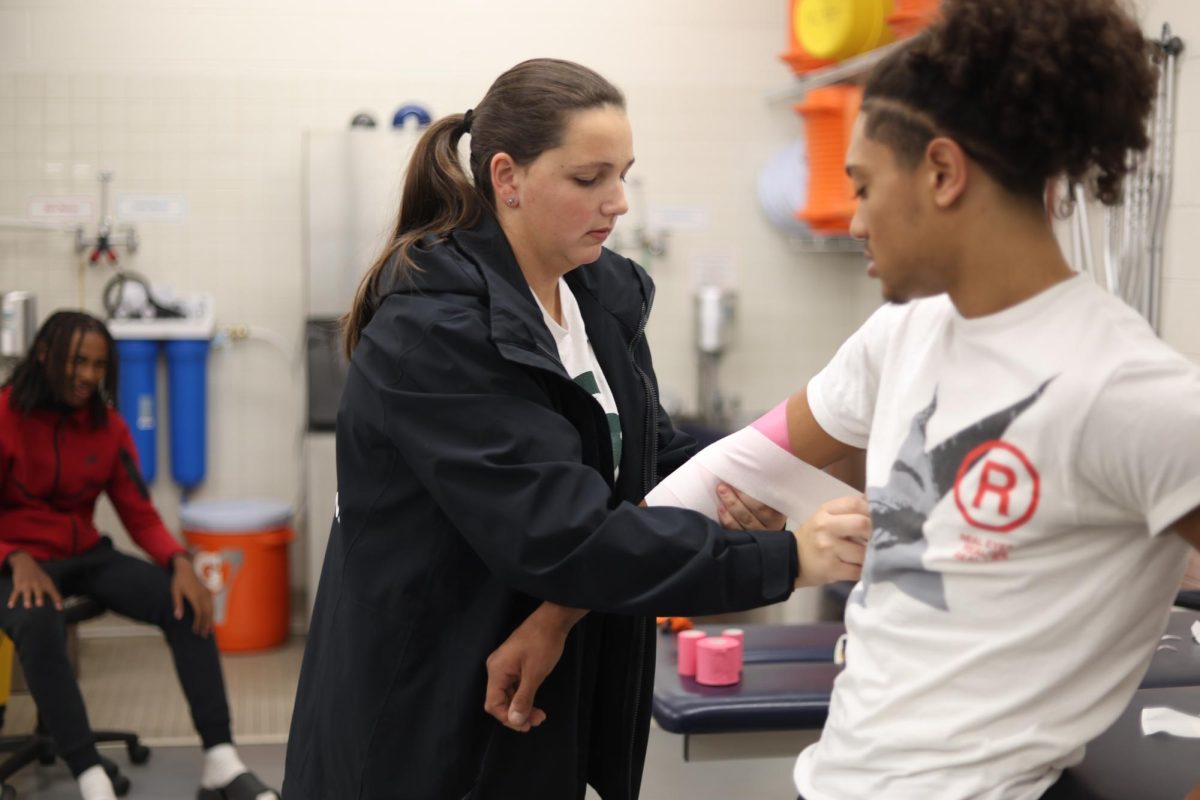 Athletic trainer Hannah McConnell wraps football player Grover Patterson's (12) arm before practice on Nov. 4. Many athletes see McConnell to prevent or treat sports injuries.