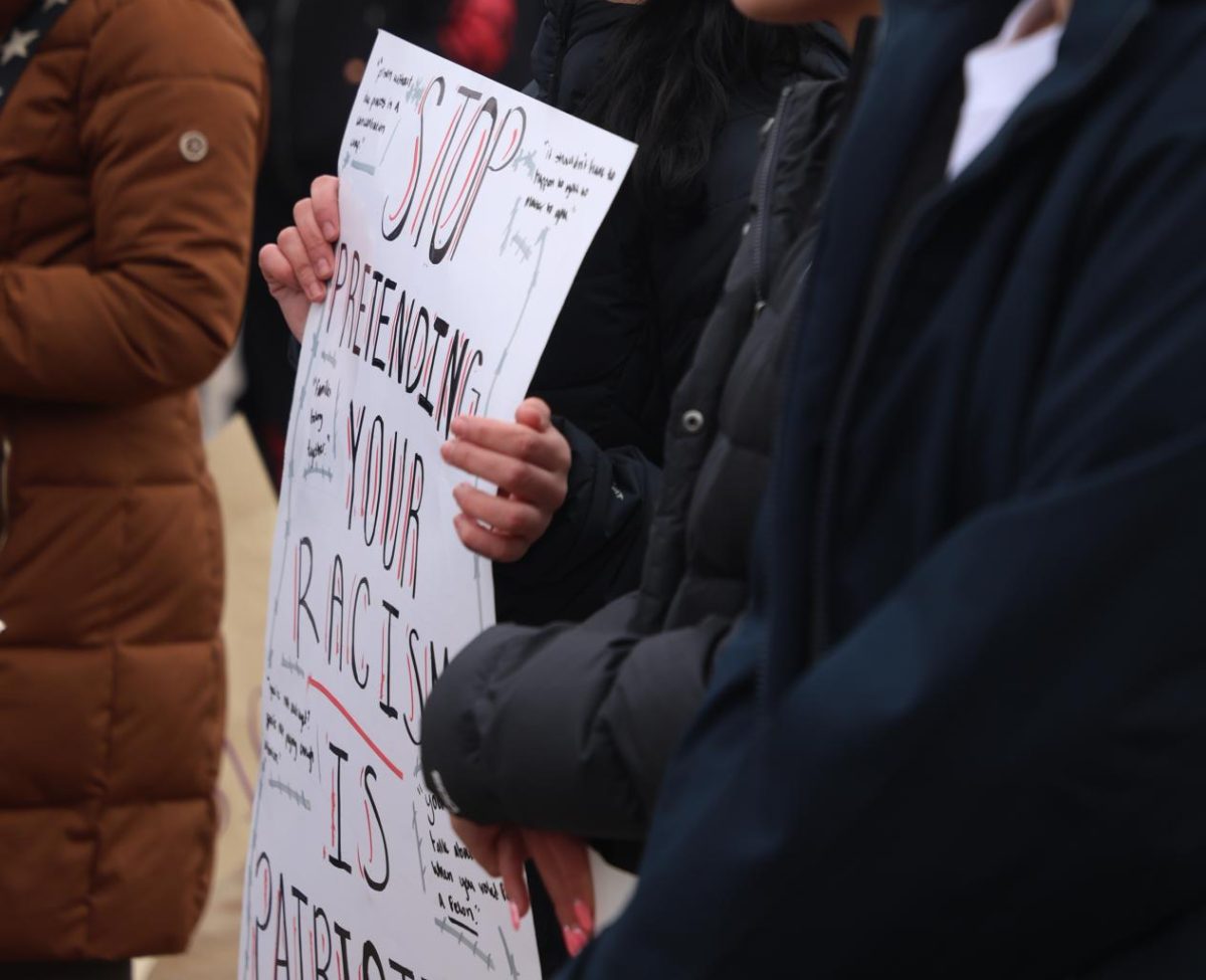 Holding a sign saying "stop pretending your racism is patriotic," Tania Dijagah (12) stands at the front of the walkout on Jan. 9. Dijagah was one of several students who spoke out at the protest against the involvement of Immigrations and Customs Enforcement (ICE) in Minneapolis.