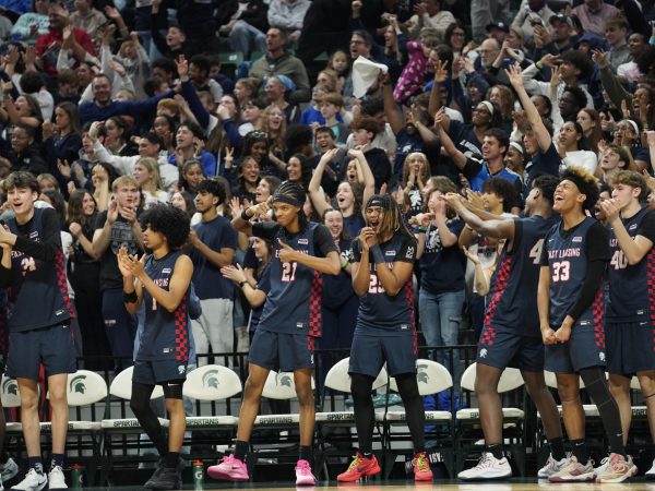 Cheering at the Mar. 14 State Finals, the boys' basketball team and the student section supports players on the court. During the semifinals, Mar. 13, school was canceled for a half day and students headed to the Breslin Center to watch. 